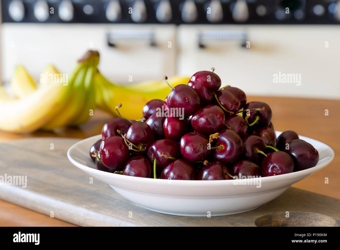 Nahaufnahme einer weißen Keramikschale, die mit glänzenden, roten Kirschen überhäutet ist. Obstschale auf dem britischen Küchentisch. Essen, Obst Fotografie. Stockfoto