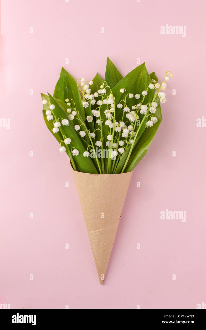 Festliche Blume Maiglöckchen Zusammensetzung in Handwerk Horn auf dem Pastell rosa Hintergrund. Ansicht von oben, Mai - lily Blumenstrauß Stockfoto