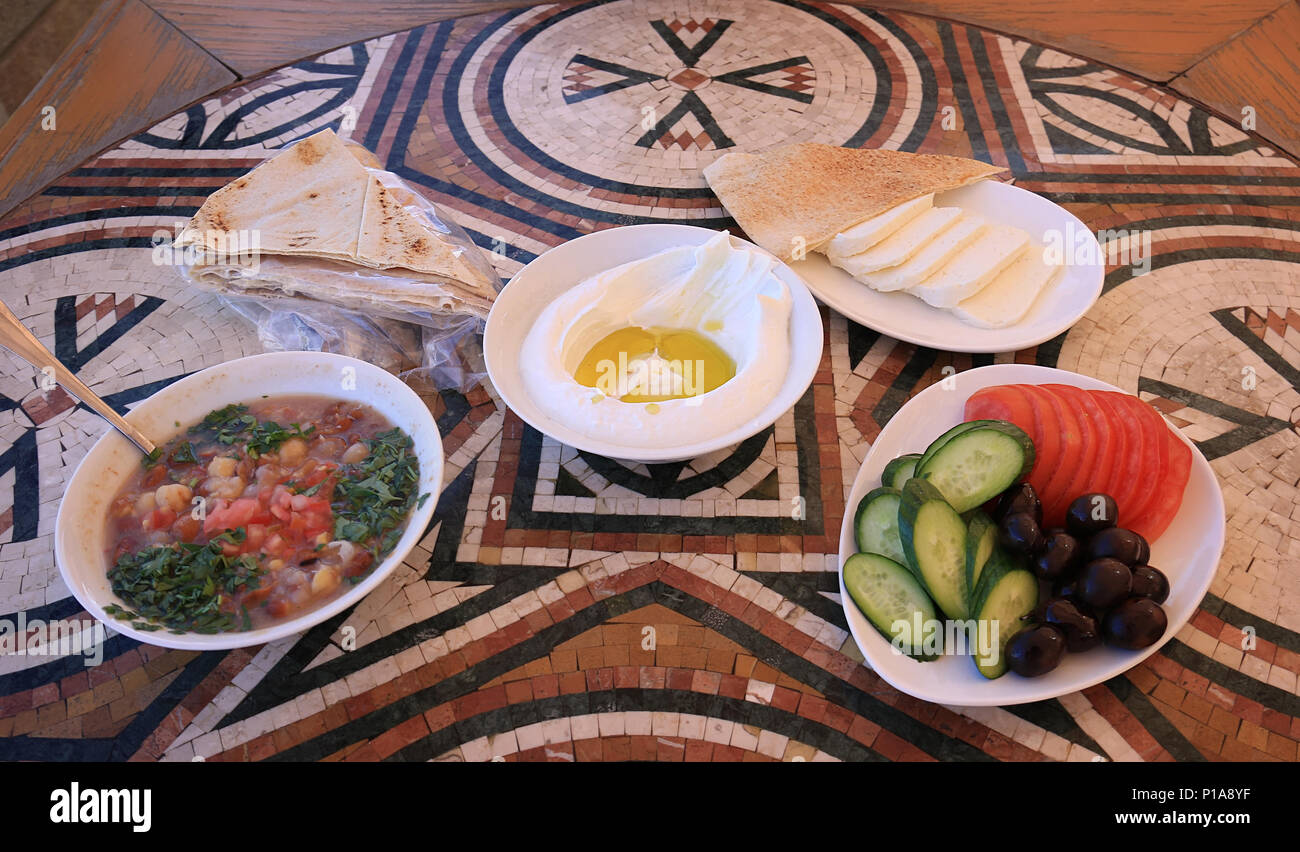 Ein libanesisches Frühstück Setup auf einem Mosaik Tisch. Die verschiedenen Gerichte sind Labneh, Foul mdammas, Halloumi Käse und Oliven, Gurken und Tomaten Stockfoto