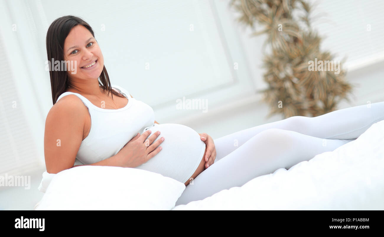 Schöne schwangere Frau am Sofa sitzen und halten Hand auf Bauch. Stockfoto