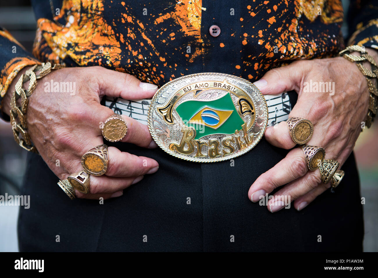 Männliche Hände mit viel souveräner Ringe holding Brasil cowboy Gürtelschnalle. Retro 70er Shirt. Stockfoto