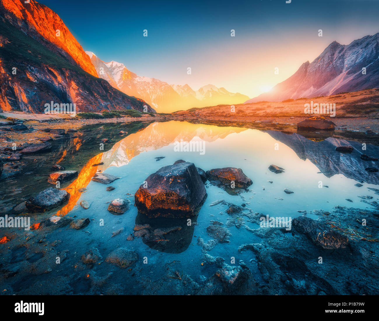 Schöne Landschaft mit hohen Bergen mit beleuchteten Gipfeln, Steine in Mountain Lake, Reflexion, blauer Himmel und gelbe Sonnenlicht im Sonnenaufgang. Nepal. Ein Stockfoto