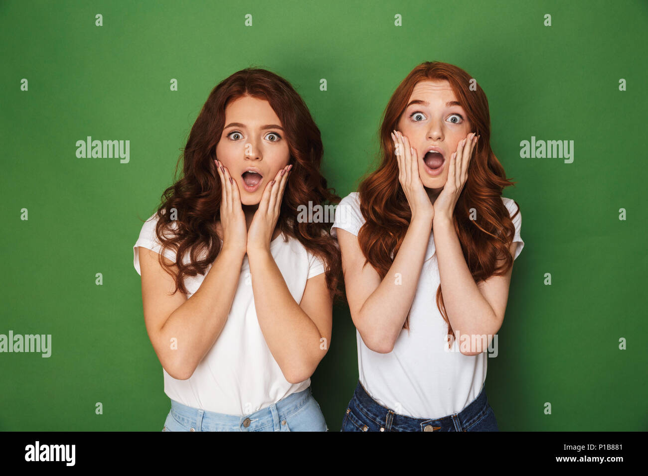 Foto von zwei kaukasischen rothaarige Frauen 20 s in Freizeitkleidung berühren Wangen mit offenen Mund und Ausbauchende Augen über grüne Hintergrund isoliert Stockfoto