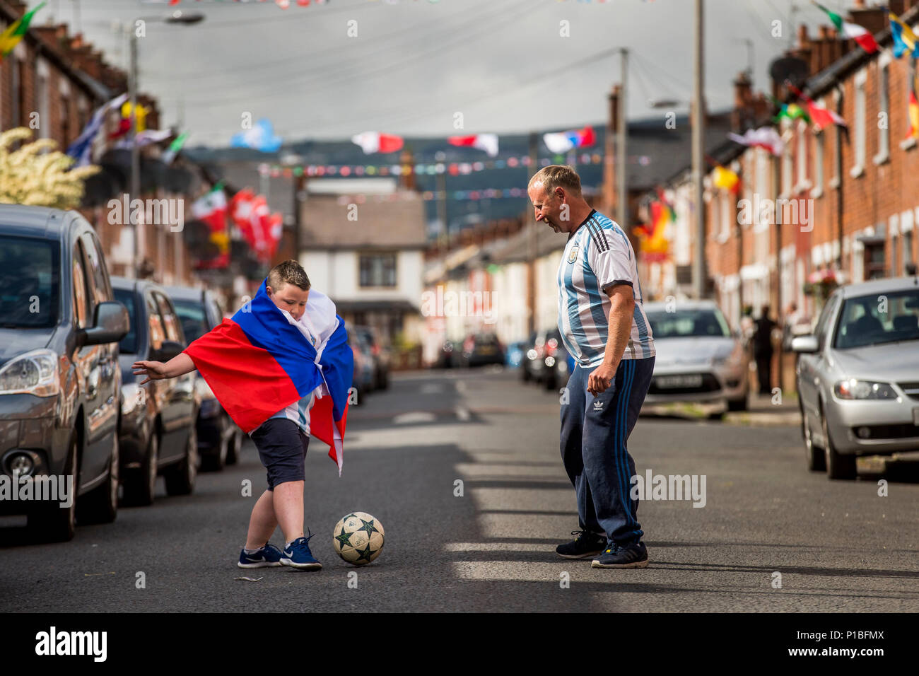 Blendenantrieb in West Belfast ansässige Sandy Turley und sein Sohn Aaron Turley spielen Fußball auf der Straße, wie er und die anderen Bewohner in das WM-Fieber ein Preisausschreiben und Kapital für ein Straßenfest am Tag des WM-Finale zu schaffen erhalten haben. Stockfoto