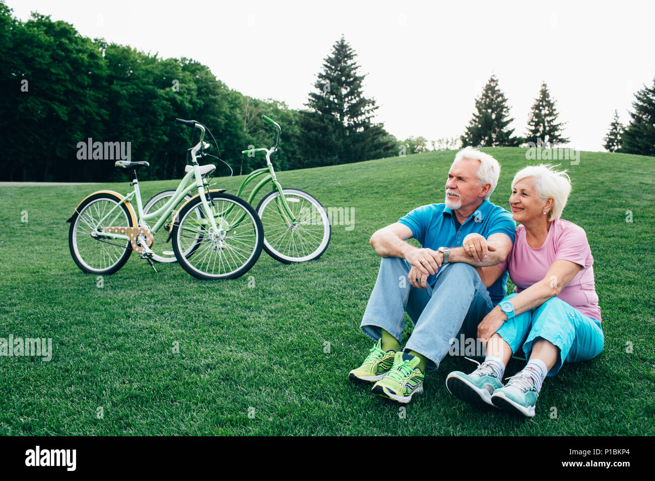 Schöne alte Paar sitzt auf dem Gras, nach dem Reiten Fahrräder Stockfoto