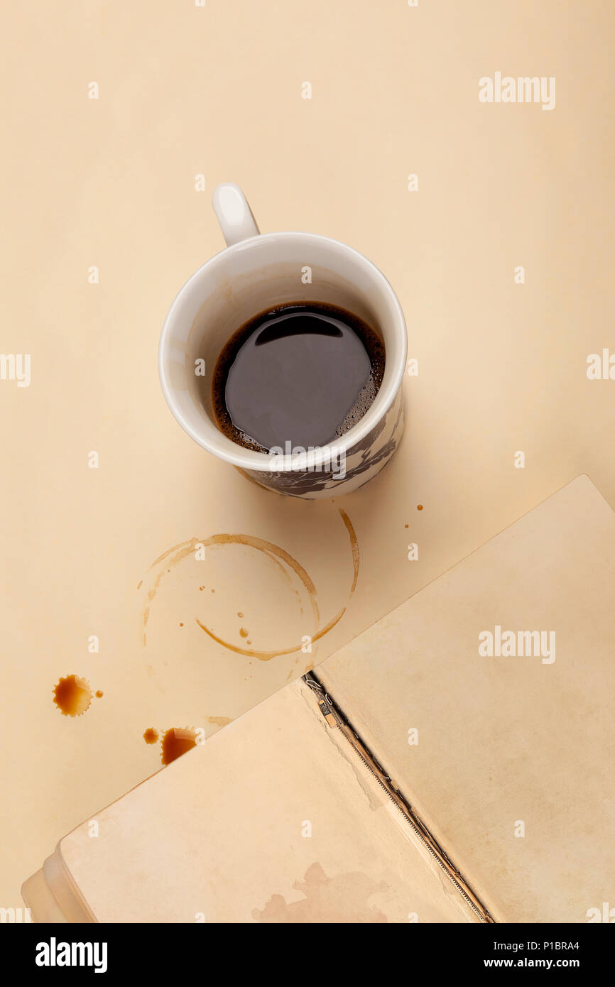 Block des Verfassers. Halb leeren Tasse Kaffee und altes Buch mit leeren Seite auf beige Tabelle mit Kaffeeflecken. Stockfoto