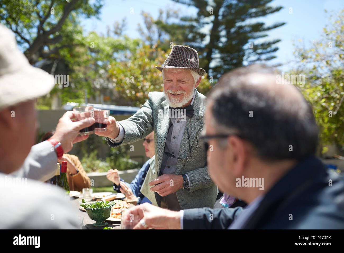 Älterer Mann in Anzug und Fliege toasten Freunde mit Wein bei Sunny Garden Party Stockfoto