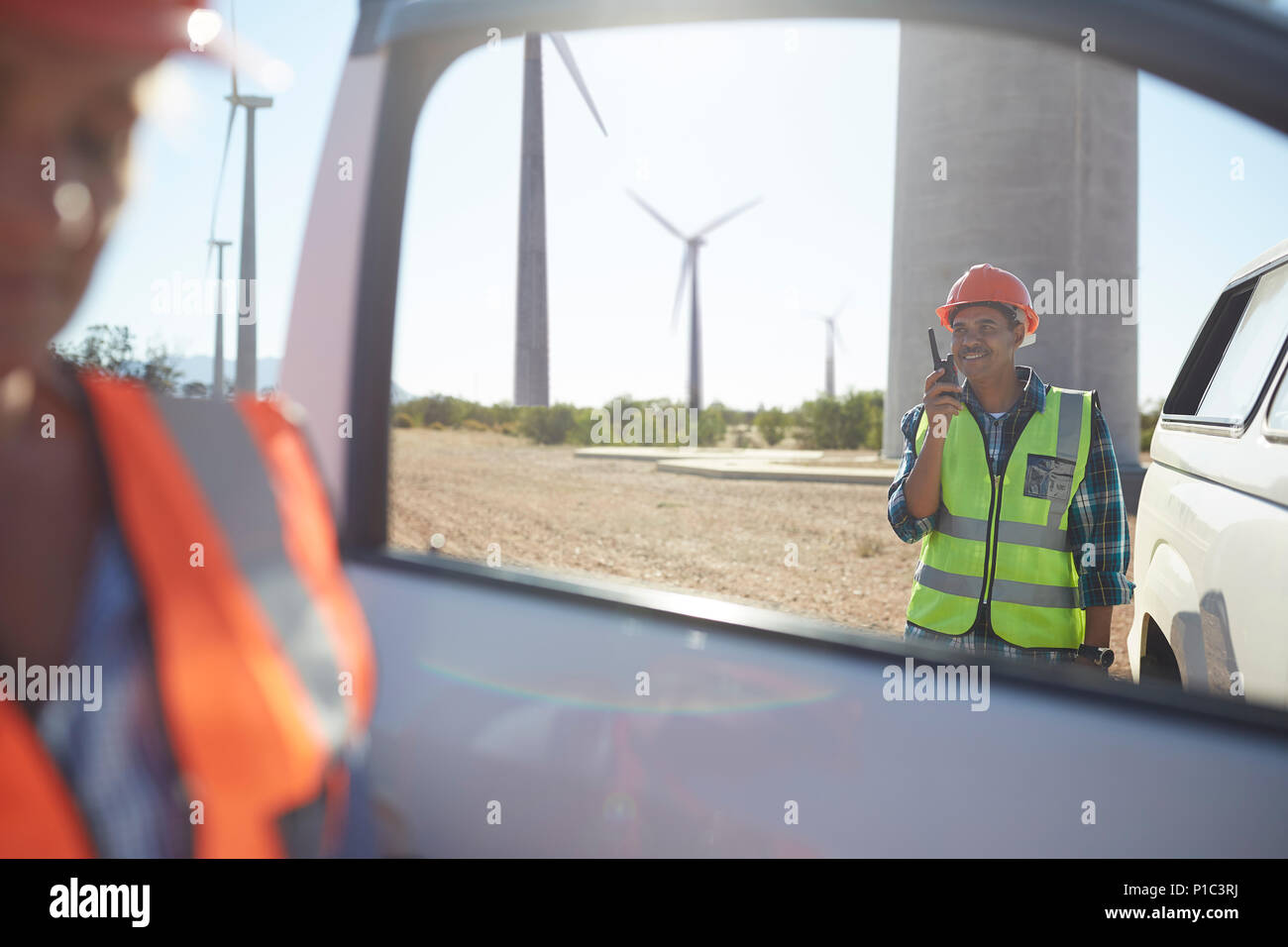 Lächelnd Ingenieur mit walkie-talkie bei Fahrzeug bei Sunny Windenergieanlage Kraftwerk Stockfoto