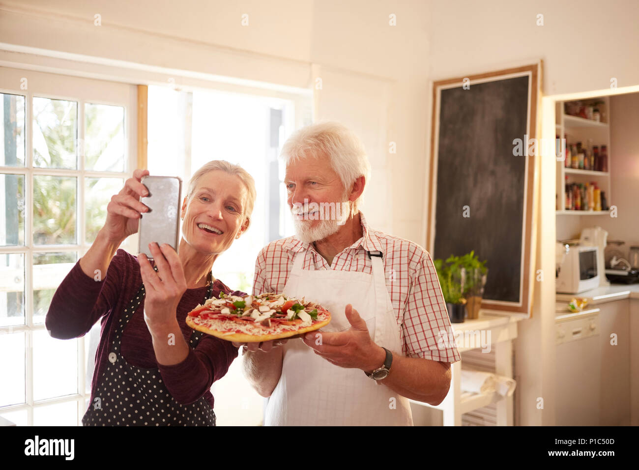 Lächelnd, zuversichtlich senior Paar unter selfie mit Pizza im Kochkurs Stockfoto