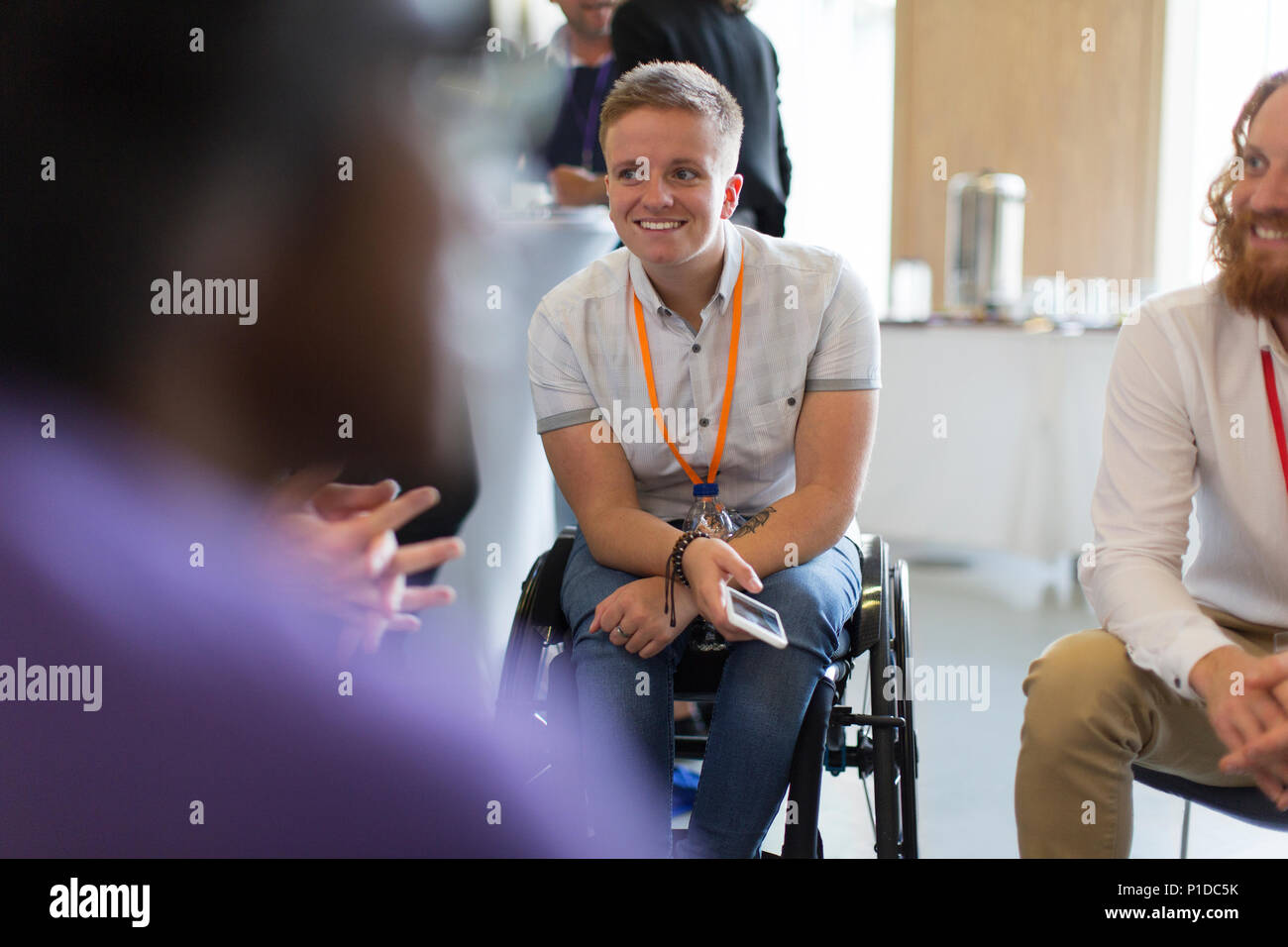 Lächelnde Frau im Rollstuhl im Gespräch mit Kollegen in der Konferenz Stockfoto