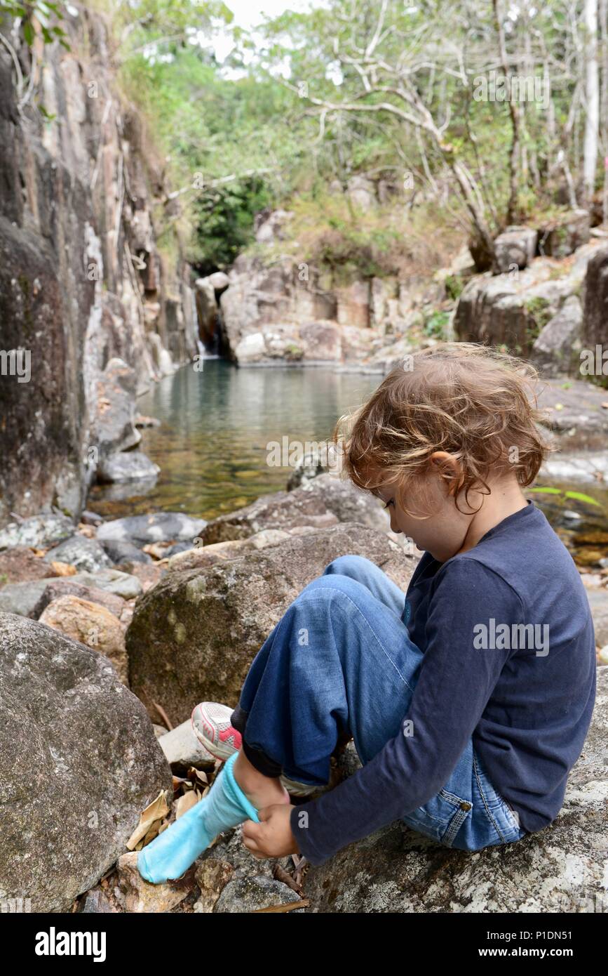 Junge Mädchen setzen auf ihre Socken und Schuhe in einer natürlichen Umgebung, Paluma Range National Park, Rollingstone QLD, Australia Stockfoto