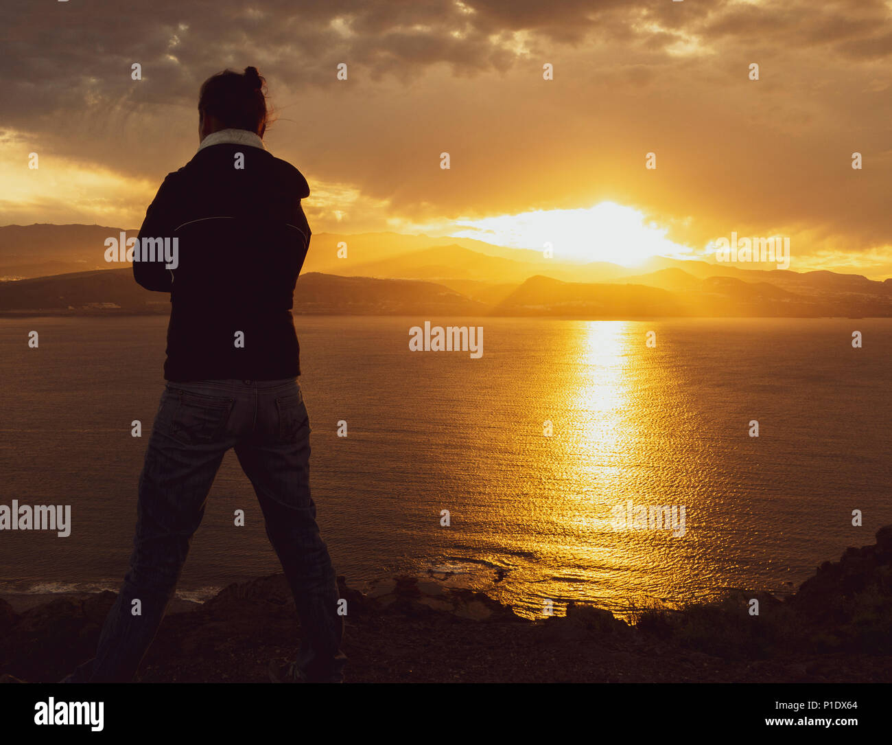 Rückansicht der Frau mit Blick auf das Meer von hohen Klippen bei Sonnenuntergang. Weibliche psychische Gesundheit/Depression, psychische Krankheit, Einsamkeit..., Konzept Bild Stockfoto