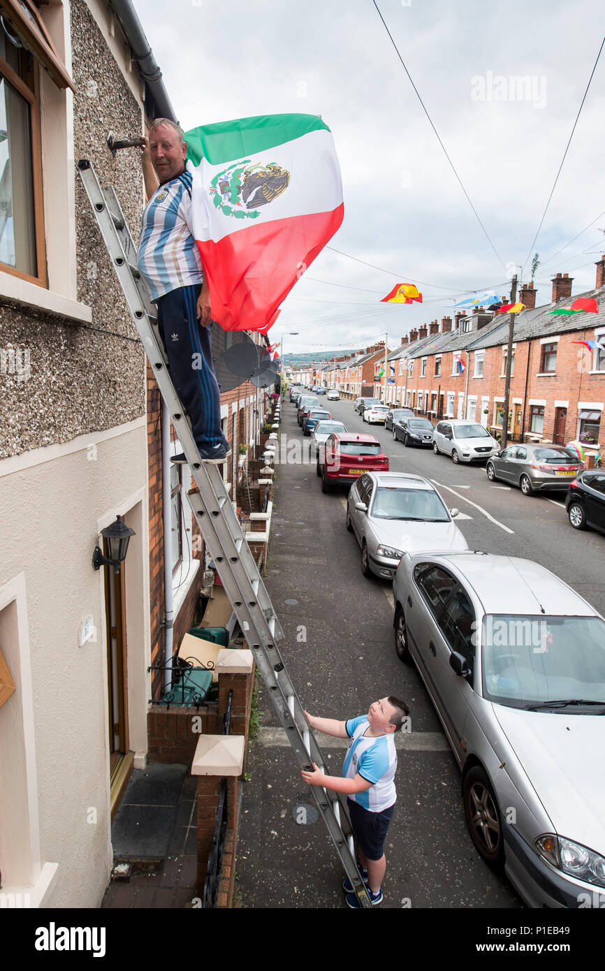 Sandy Turley Buchung der Mexikanischen Flagge sein Zuhause bei Iris in West Belfast mit Hilfe seines Sohnes Aaron Turley, wie er und die anderen Bewohner in das WM-Fieber ein Preisausschreiben und Kapital für ein Straßenfest am Tag des WM-Finale zu schaffen erhalten haben. Stockfoto