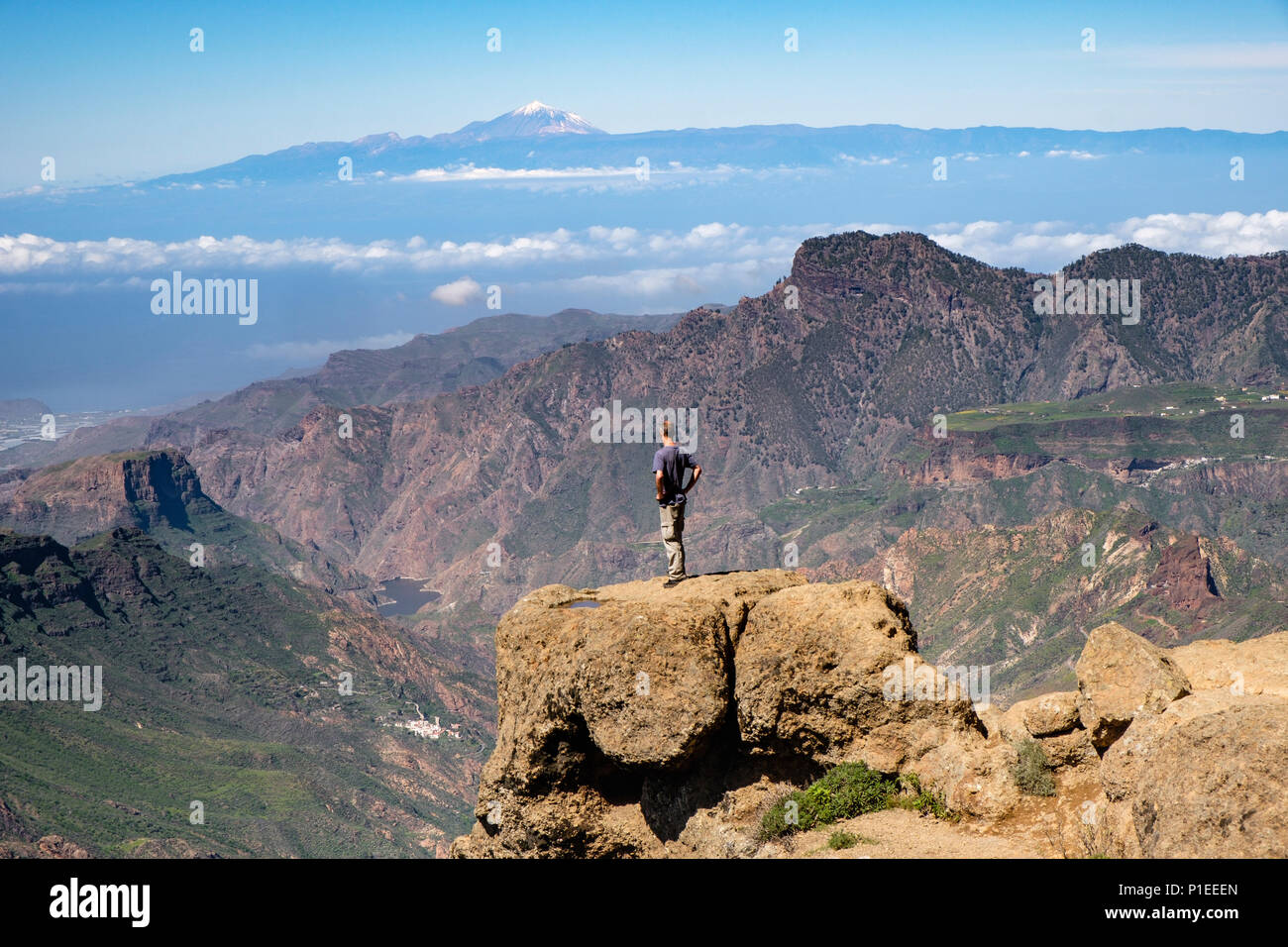 Mann sieht von Roque Nublo über die bergige Land von Gran Canaria auf den Vulkan Teide, Gran Canaria, Kanarische Inseln, Spanien Stockfoto