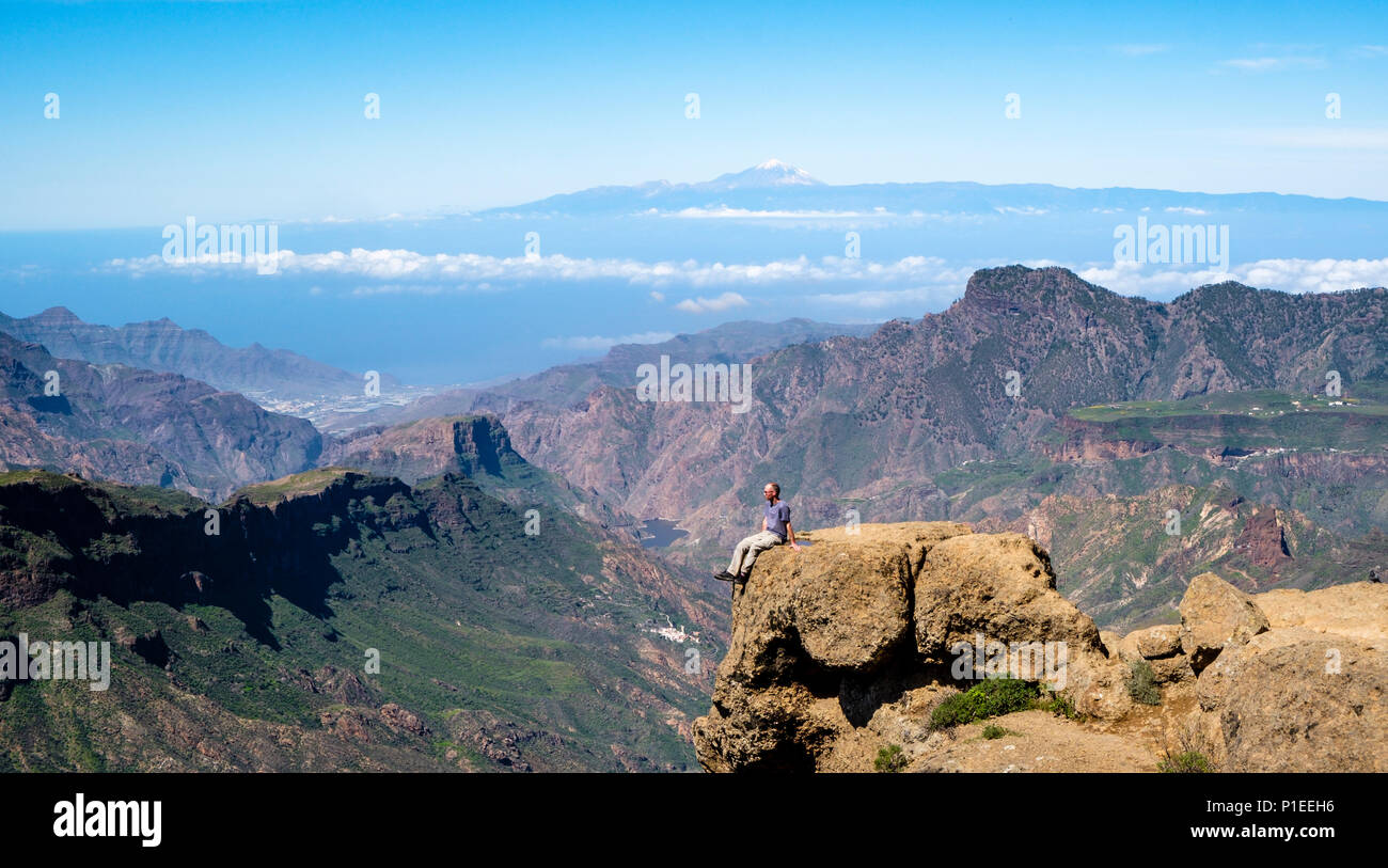 Mann sieht von Roque Nublo über die bergige Land von Gran Canaria mit Vulkan Teide am Horizont, Gran Canaria, Kanarische Inseln, Spanien Stockfoto