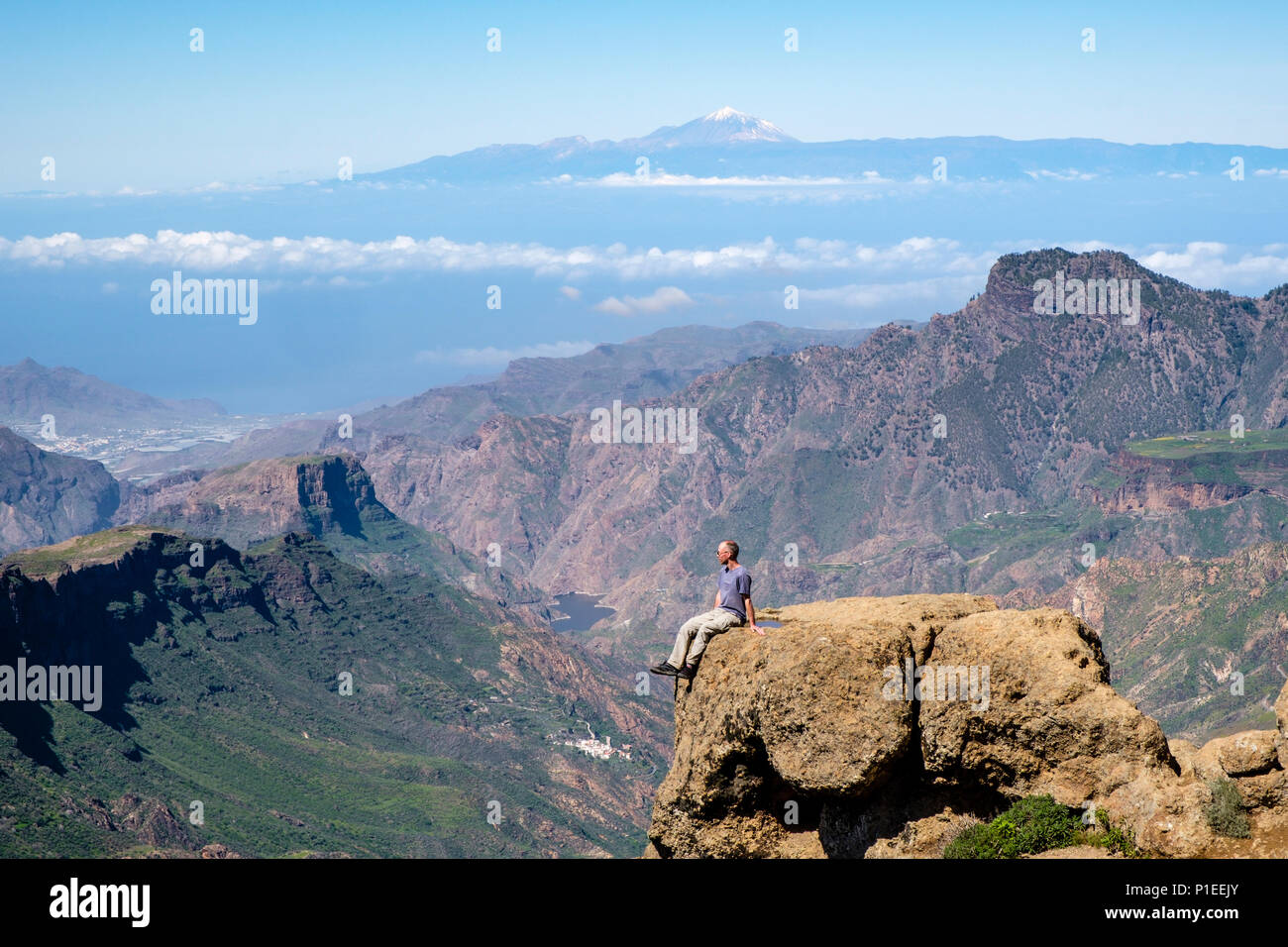 Mann sieht von Roque Nublo über die bergige Land von Gran Canaria mit Vulkan Teide am Horizont, Gran Canaria, Kanarische Inseln, Spanien Stockfoto