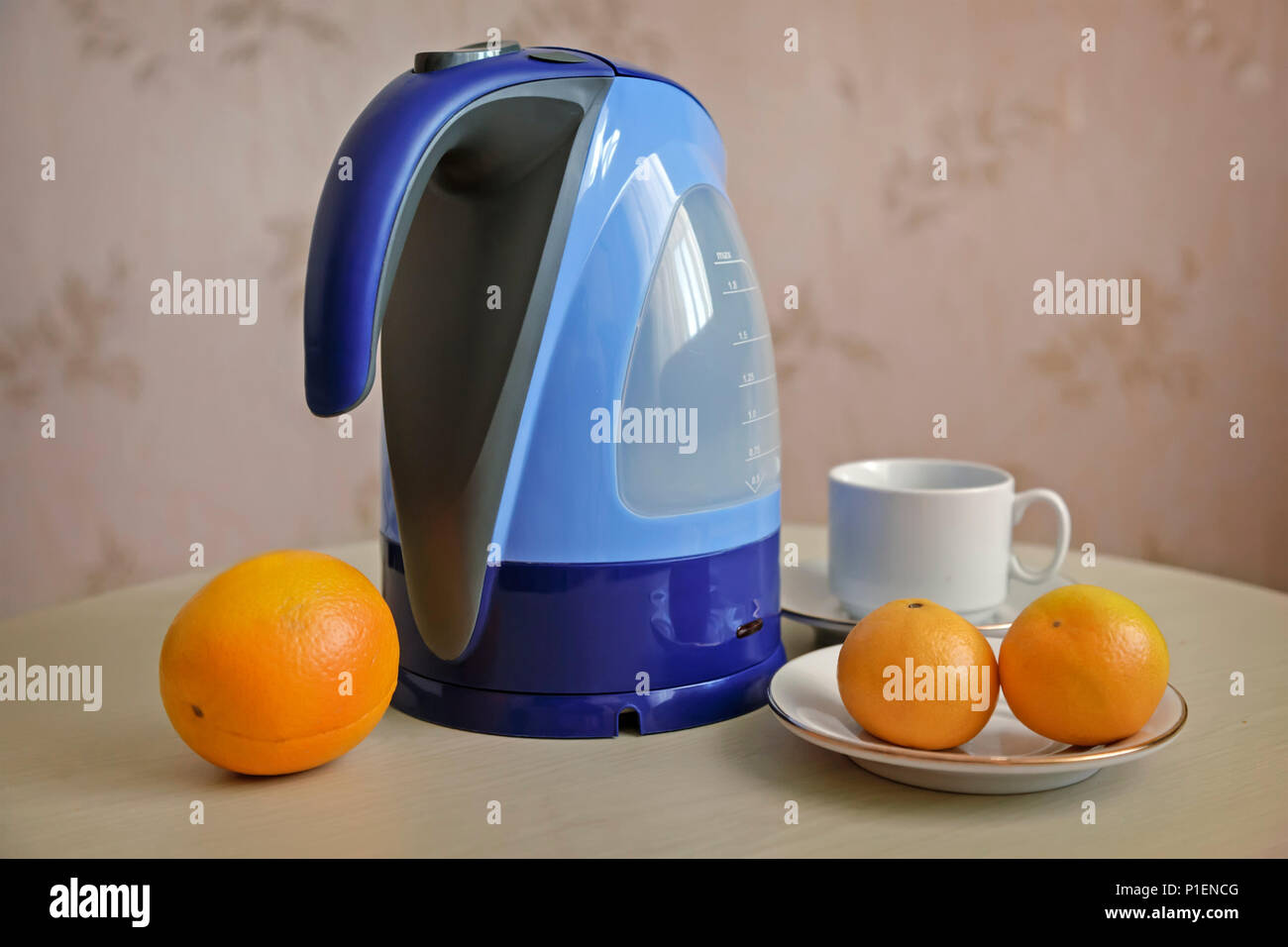 Auf dem Tisch ist ein Wasserkocher, nächsten sind Orangen und Mandarinen. Stockfoto