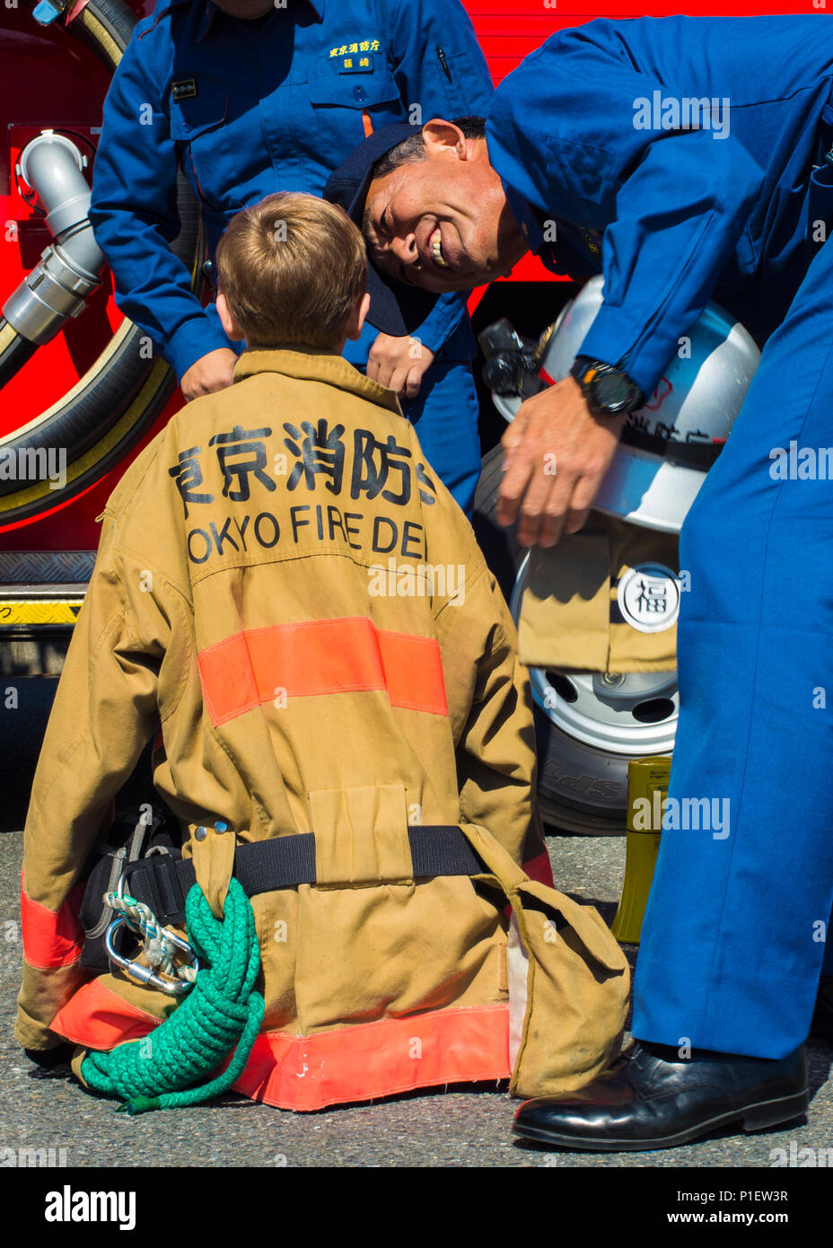 Feuerwehrleute der Tokioter Feuerwehr helfen einem Kind während der Brandverhütungswoche im Yokota Community Center, Japan, beim Anprobieren von Brandschutz-Ausrüstung. Bei der Veranstaltung werden Feuerwehrausrüstung der 374th Civil Engineer Squadron und der Japan Air Self-Defense Force Fire and Rescue gezeigt. Die Aktivitäten fördern Brandsicherheitsschulungen, Notfallvorsorge, Engagement in der Gemeinde, Bewusstsein für Schutzausrüstung, Betriebsverfahren und Teamarbeit zwischen US-amerikanischem und japanischem Personal. Stockfoto