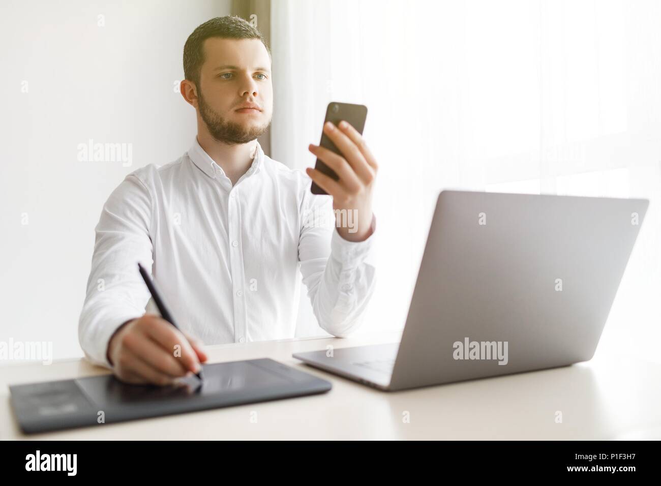 Junge lächelnde bärtigen Geschäftsmann ist Arbeiten am Computer, Smartphone. Stockfoto