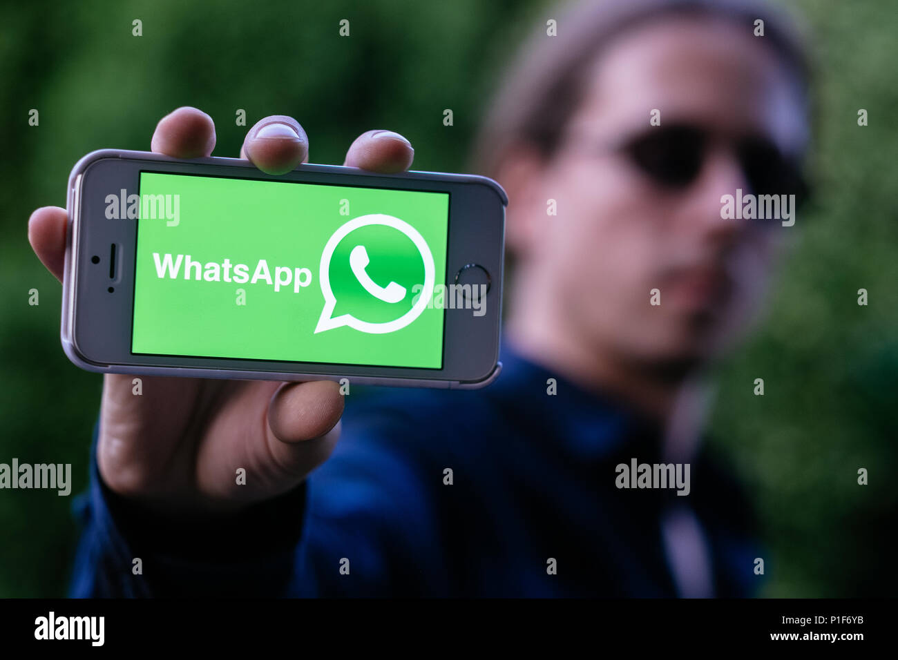 Nahaufnahme der coole junge Mann mit weißen iPhone mit WHATSAPP Logo auf dem Bildschirm Stockfoto