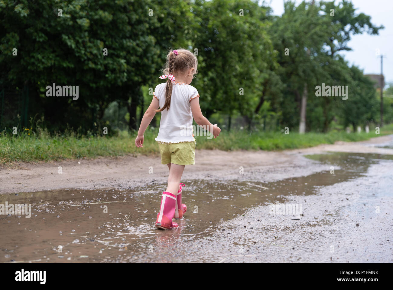 Kleine Mädchen zu Fuß entlang der nassen gebrochen Straße nach dem Regen. Geschichten über das ländliche Leben in der Ukraine Stockfoto