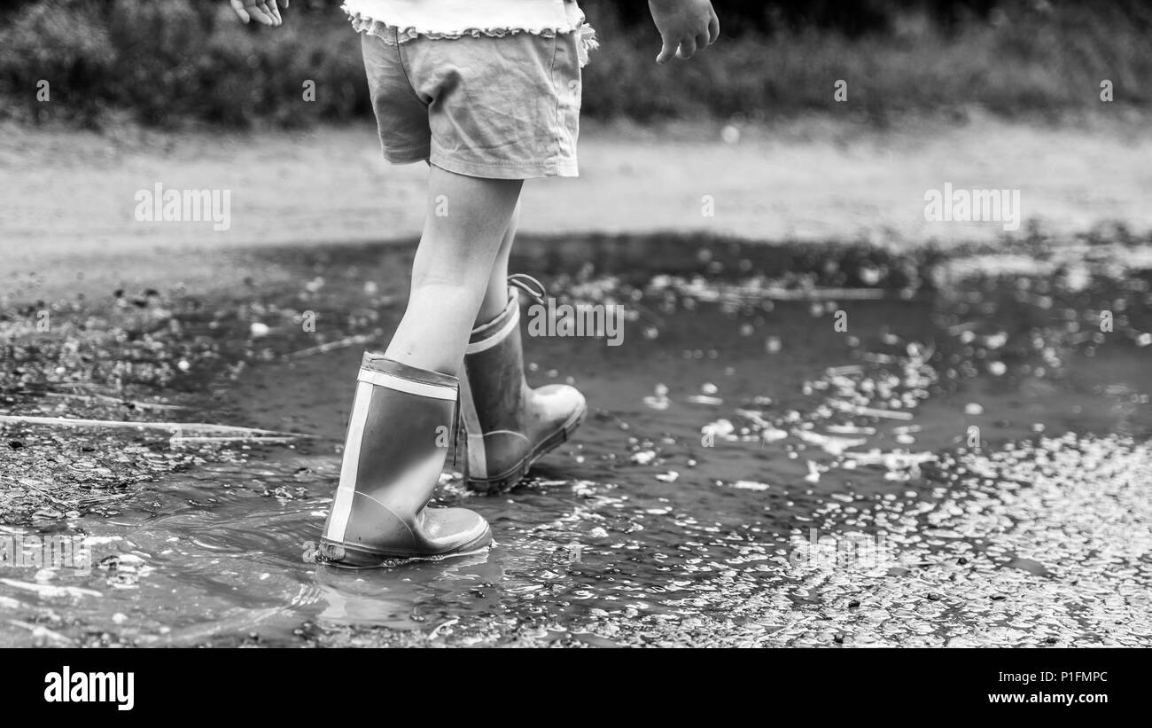 Kleines Mädchen in Gummistiefeln entlang das Wasser nach dem Regen, Straße, Landschaft, Schwarzweiß-Effekt ruiniert. Geschichten über das ländliche Leben in der Ukraine Stockfoto