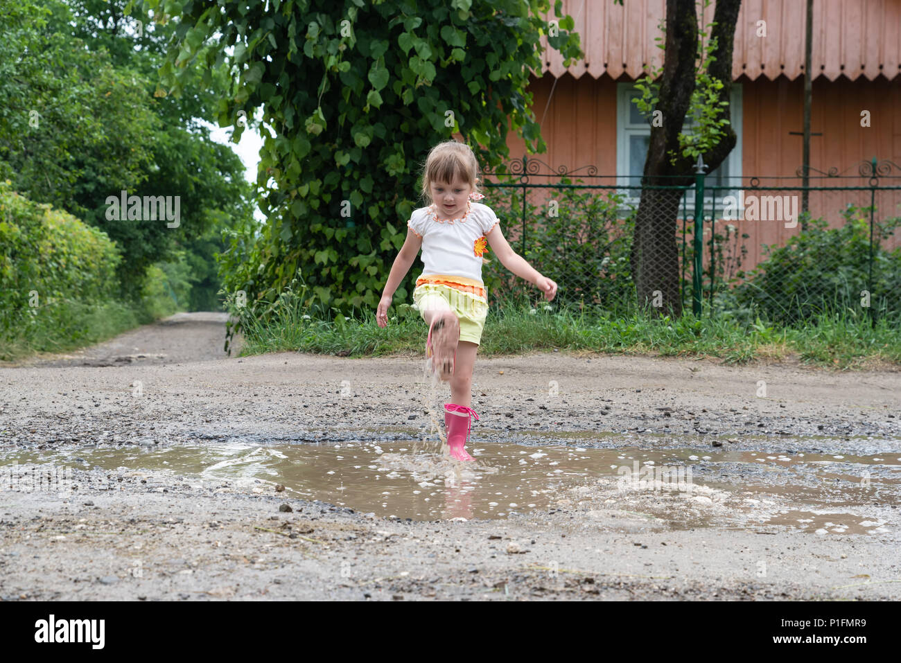 Kleine Mädchen spielen im Wasser in der Mitte eines zerstörten Straße, nach Regen. Geschichten über das ländliche Leben in der Ukraine Stockfoto