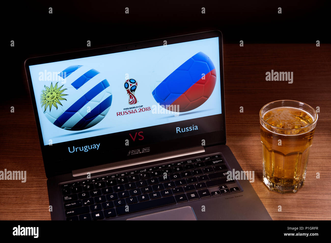 Die uruguayische und Russische Fahnen zusammen gesehen mit der Russischen WM-Logo 2018 angezeigt auf einem Laptop neben einem Glas Bier. Dieses Spiel gehört zu den ersten Match up aus der Gruppe A und wird in Samara, Russland gespielt werden. Stockfoto
