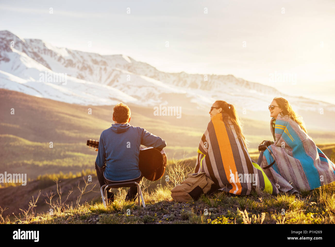 Drei glückliche Freunde spielt Musik von Gitarre gegen die Berge und den Sonnenuntergang. Für text Stockfoto