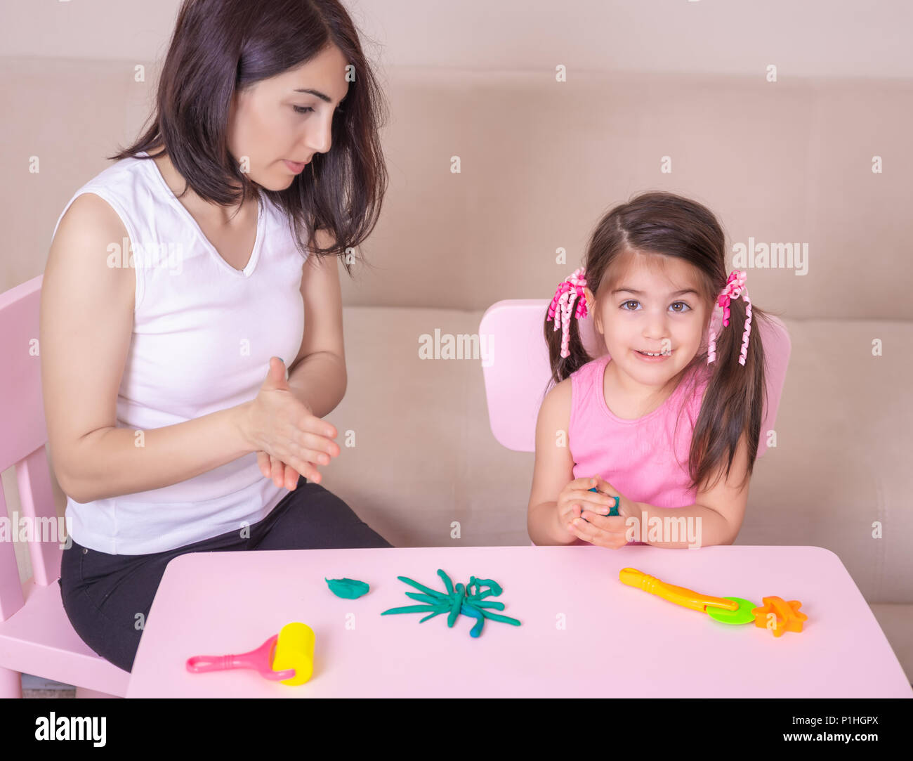 Schönen Mutter und nettes Mädchen spielen zusammen mit Knetmasse, beim Sitzen am Tisch. Stockfoto
