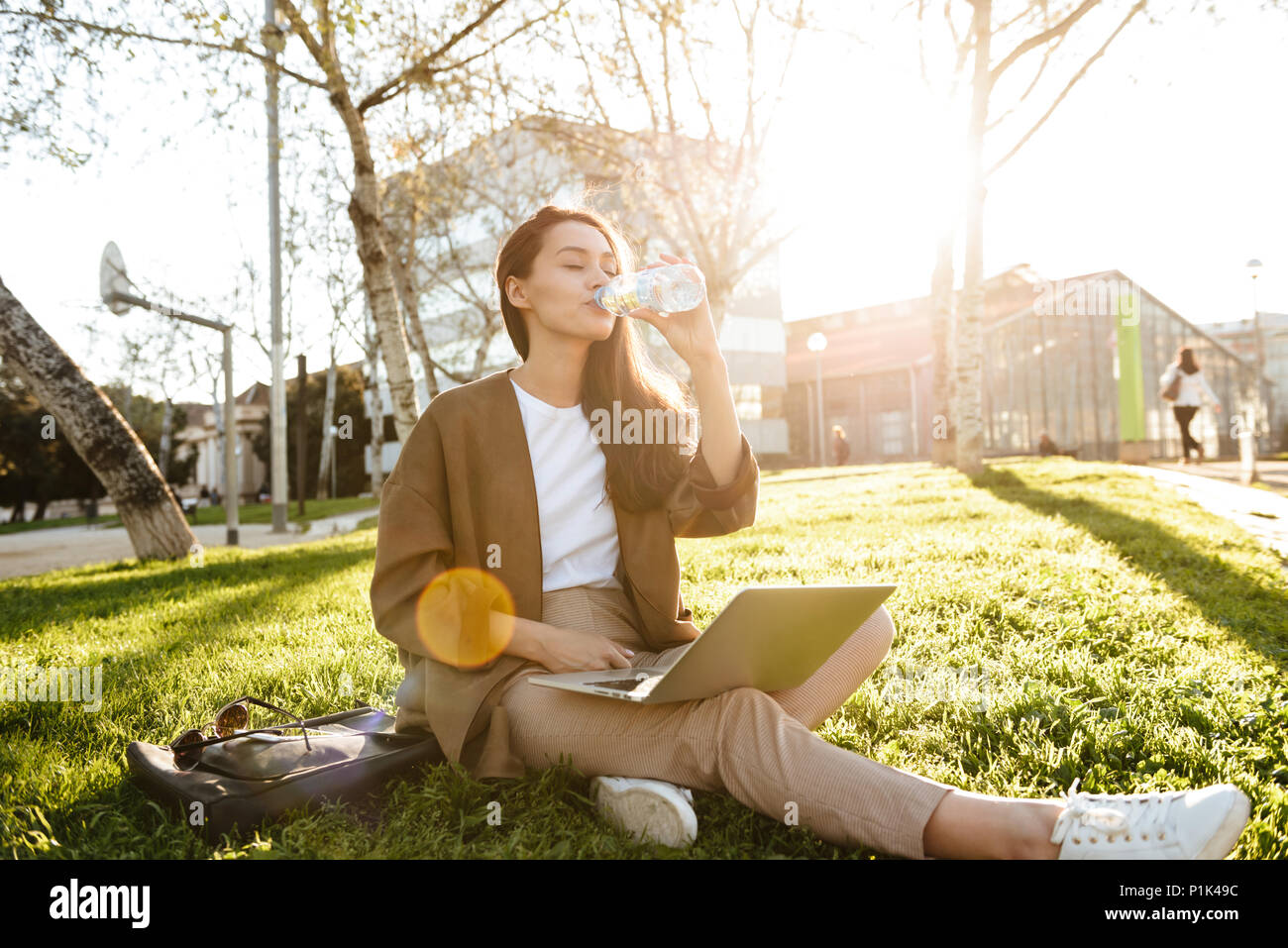 Bild von erstaunlich schöne Frau sitzt auf Gras im Freien Trinkwasser mit Laptop Computer. Stockfoto