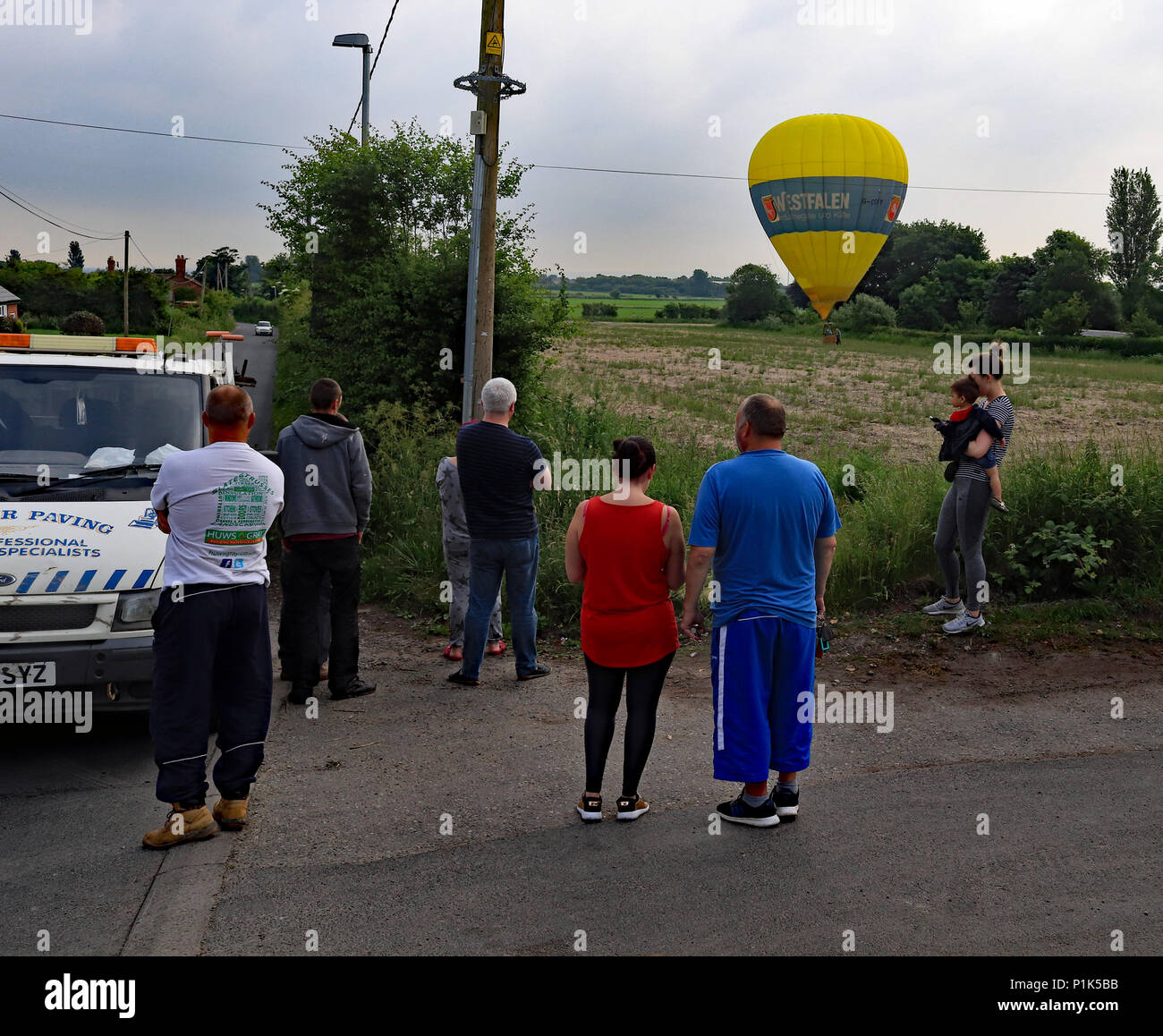 Eine kleine Menge Uhren auf als große gelbe Heißluftballon landet im Feld eines Bauern in der Nähe des Dorfes Burscough in West Lancashire. Stockfoto