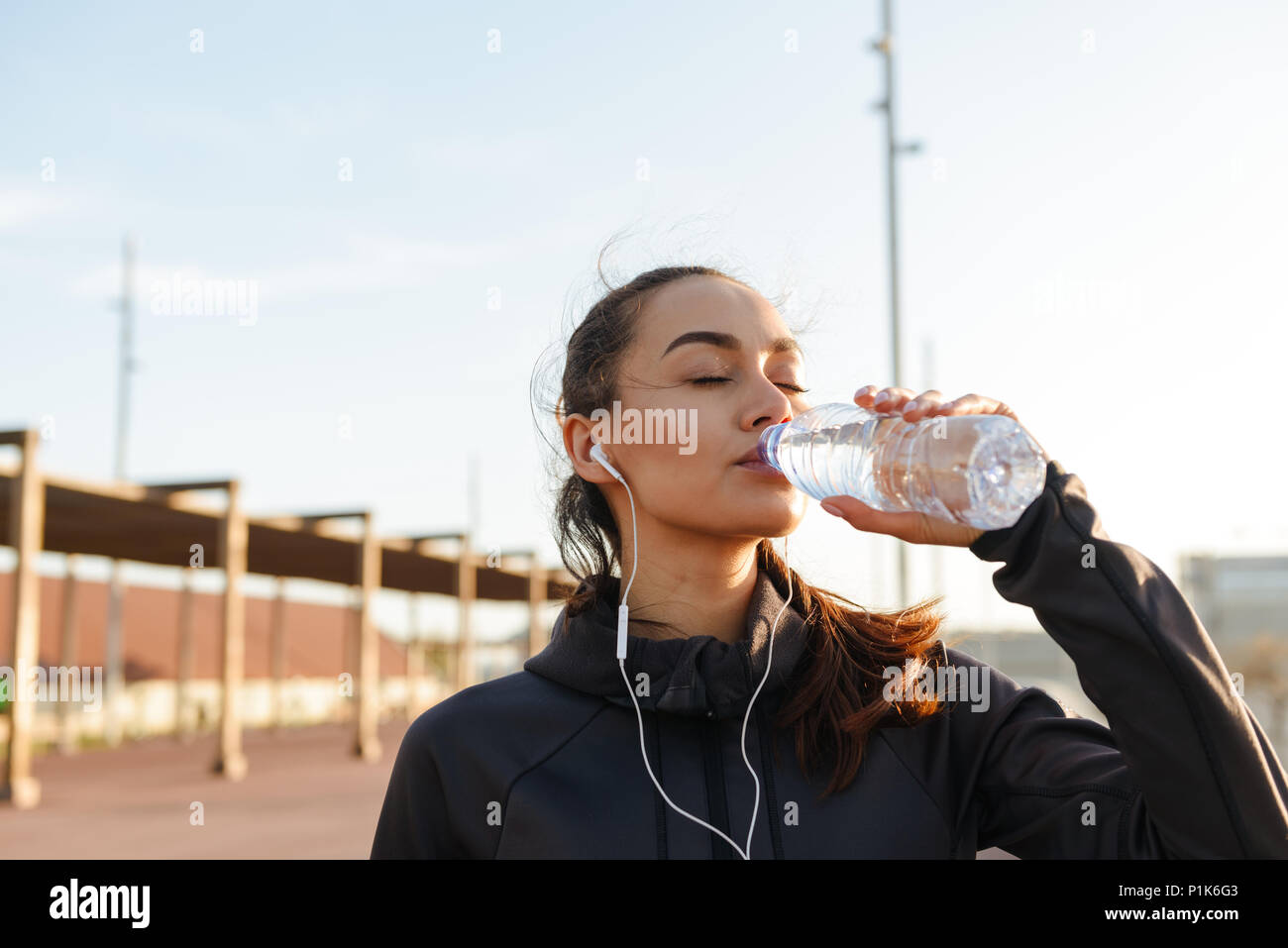 Bild von schönen jungen asiatischen Sport Frau Musik hören mit Kopfhörern Trinkwasser im Freien. Stockfoto