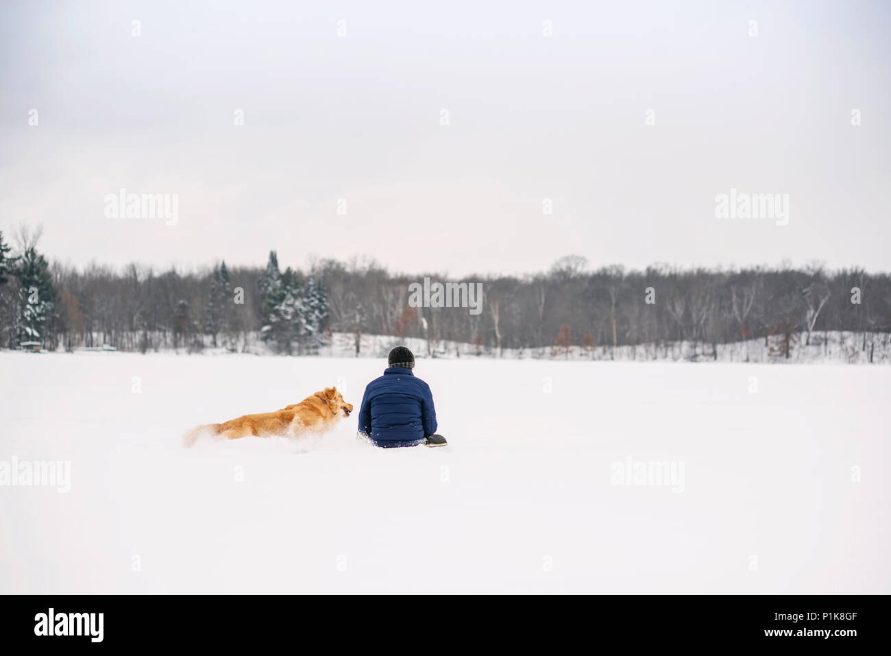 Mann sitzt im Schnee mit seinem Golden Retriever Hund Stockfoto