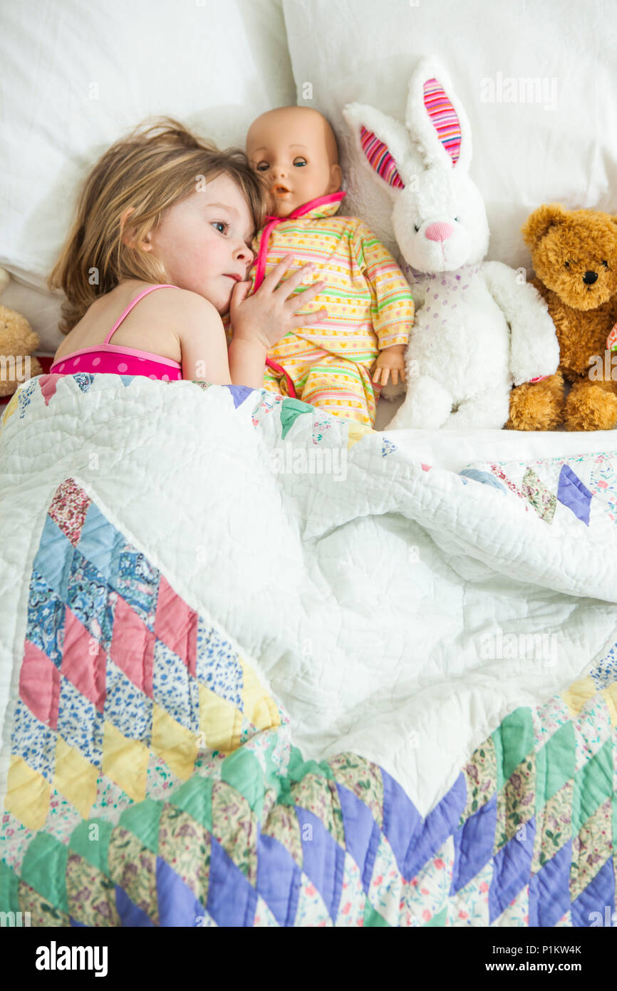 Kleines Mädchen versteckt sich im Bett mit ihrem Spielzeug. Stockfoto