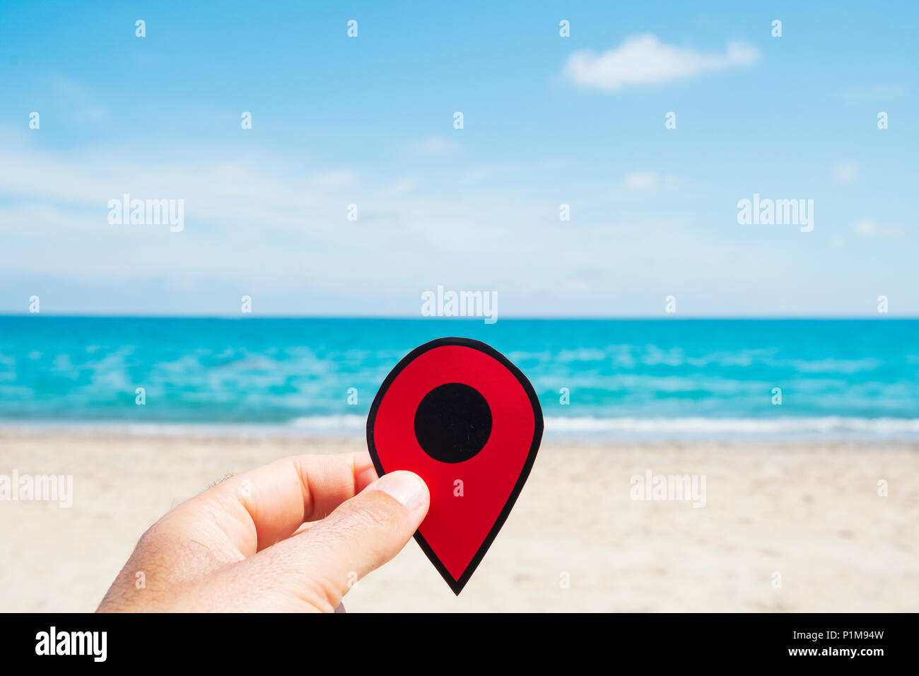 Nahaufnahme eines jungen kaukasischen Mann mit einem roten Marker in der Hand, entspannt am Strand, mit dem Meer im Hintergrund Stockfoto