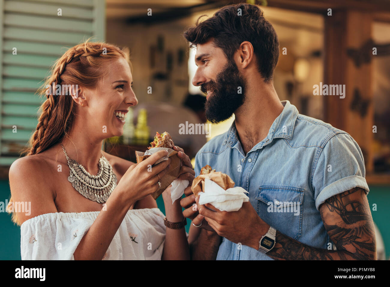 Portrait von glückliches junges Paar Burger im Freien. Junger Mann und Frau, die in der Nähe von einem Lebensmittel Lkw und Burger essen. Stockfoto