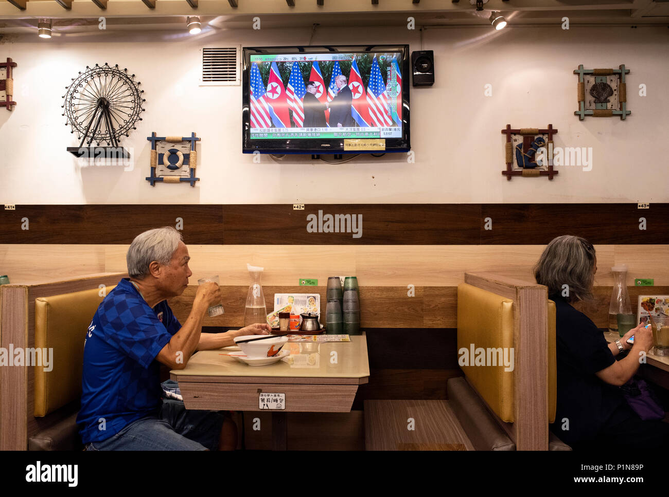 In einem lokalen Restaurant in Hongkong, einem lokalen Uhren ein TV-Bildschirm  angezeigt, der die historischen Moment, wenn US-Präsident Donald Trump und  Nordkorea Kim Jong-un zum ersten Mal während der Singapur Frieden erfüllen