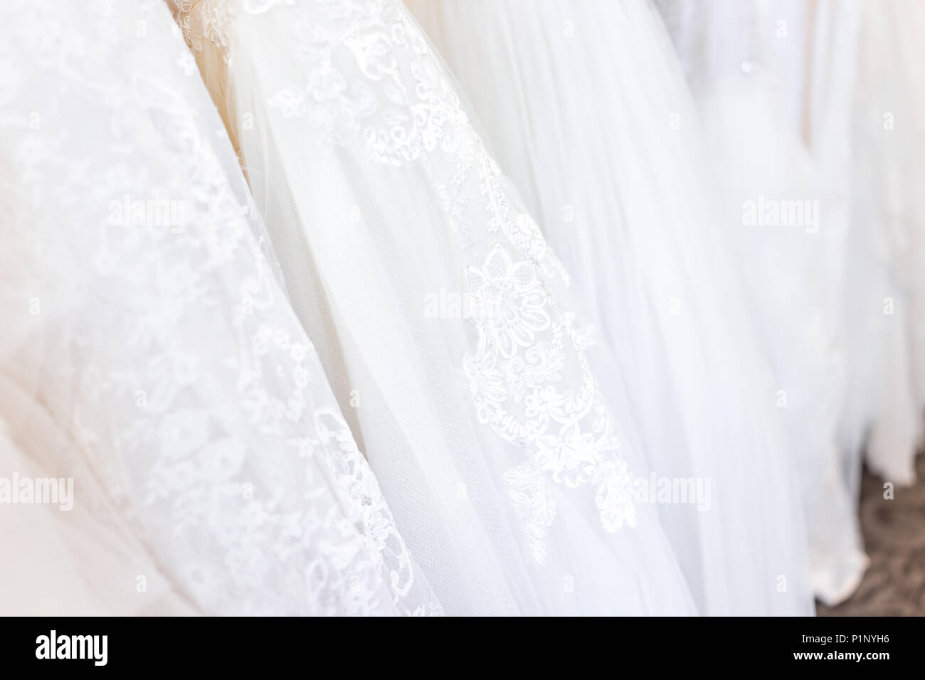 Viele Brautkleider auf Rack in Boutique Diskontgeschäft, weiße Kleider hängen Aufhänger Reihe Nahaufnahme mit weißer Spitze, Tüll, Design Stockfoto