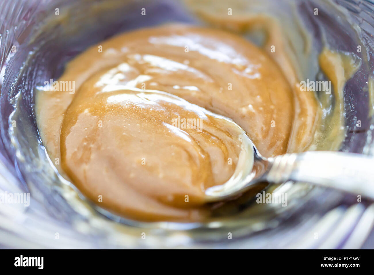 Makro Nahaufnahme von Golden Brown Caramel Sauce mit Löffel dicke klebrige süße Nachspeise gesüßte Kondensmilch Sirup in der Schüssel Stockfoto