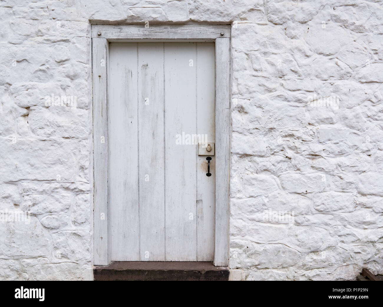 Alte Weiße verwitterten hölzernen Tür auf einem weiß getünchten Gebäude aus Stein Stockfoto
