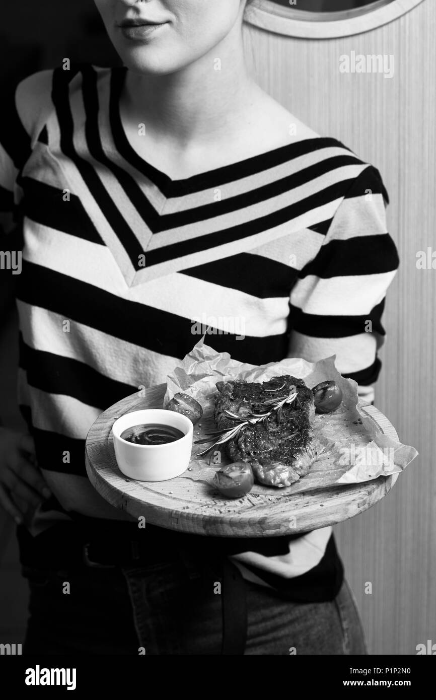 Frau gekleidet in gestreiften Pullover Holding runde Holzplatte mit appetitlichen Beteiligung mit Kirschtomaten, Rosmarin und Sauce liegen auf Stück von Kra serviert. Stockfoto