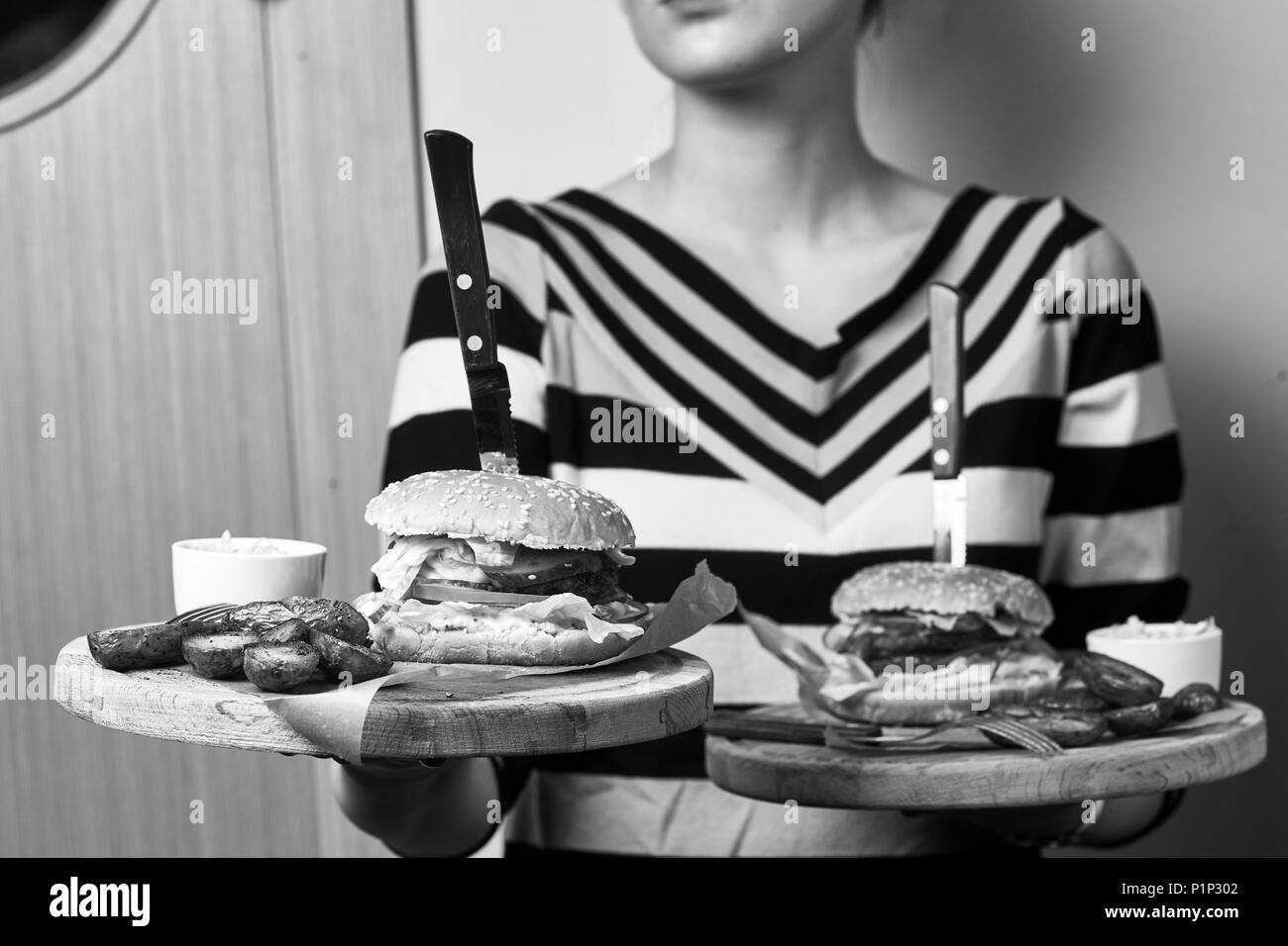 Kellnerin gekleidet in gestreiften Pullover mit Paar runden hölzernen Fächer mit leckeren Burger, Soße und Bratkartoffeln liegen auf Stücke von Kraftpapier. Stockfoto