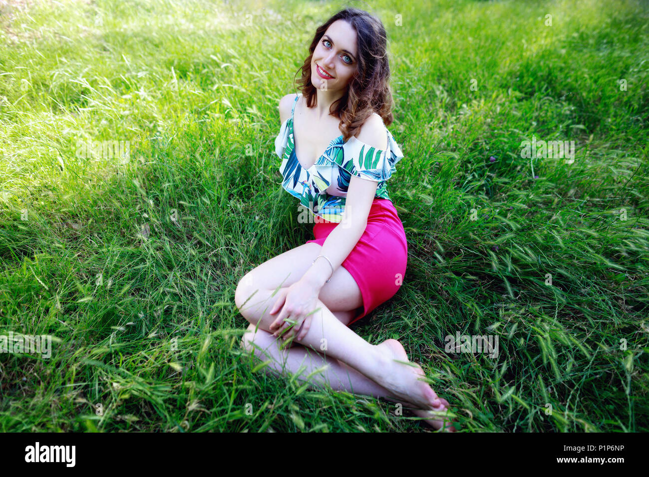 Schöne brünette Mädchen in das grüne Gras des Parks liegen, sieht in die Kamera und lächelt. Stockfoto