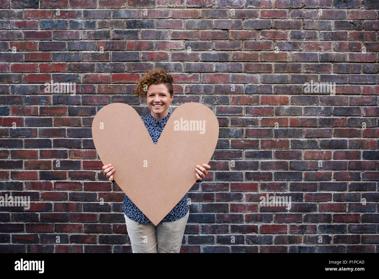 Junge Frau lächelnd und halten ein großes Herz außerhalb Stockfoto