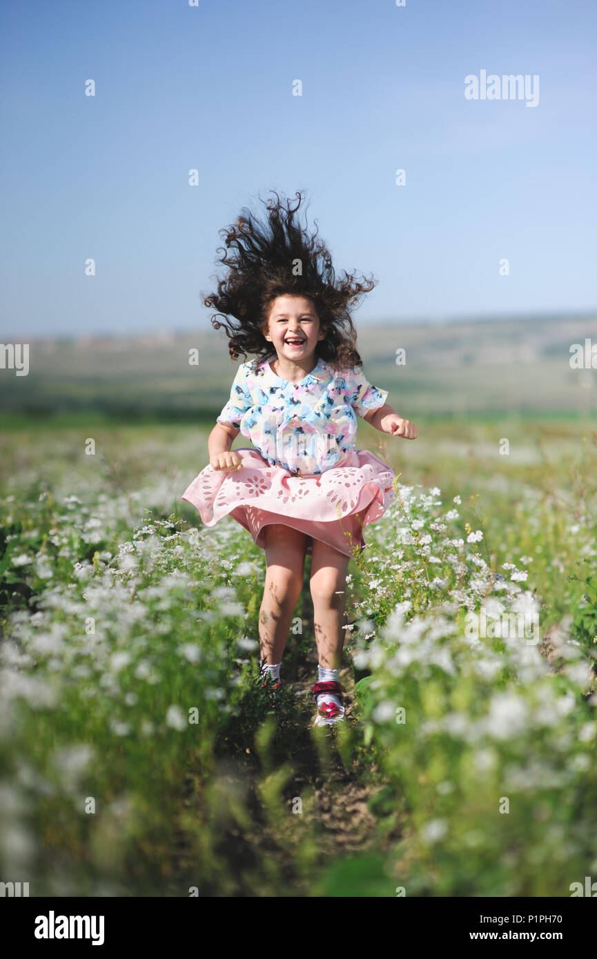 Gerne lustig Springen kleines Mädchen mit lockigem Haar Flattern unter Sommer Blume Bereich Stockfoto