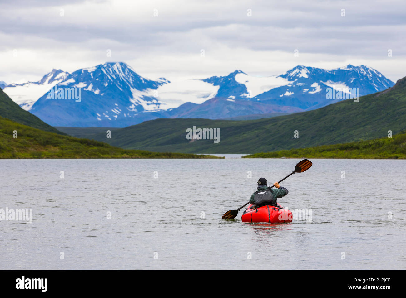 Ein Mann Paddles eine Lücke packraft über Sehenswürdigkeit Lake mit der Alaska Range in der Ferne, Alaska, Vereinigte Staaten von Amerika Stockfoto