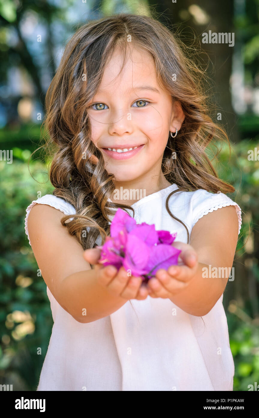 Porträt einer Kaukasischen fünf Jahre alten Mädchen lächelnd und mit violetten Blüten in einem Park als Geschenk Stockfoto