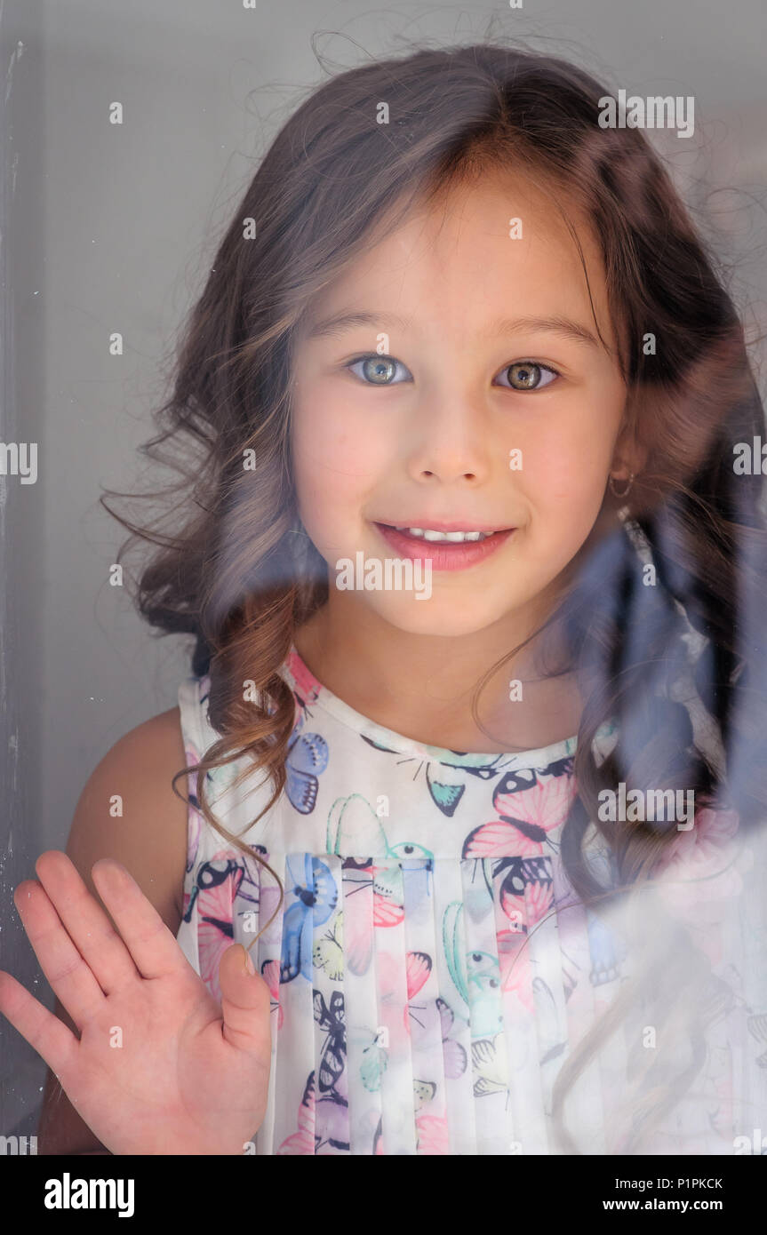 Porträt einer niedlichen kaukasischen fünf Jahre altes Mädchen hinter einem Fenster Glas lächelnd Stockfoto