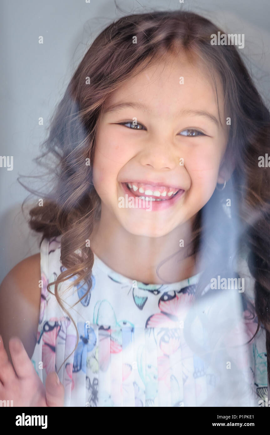 Porträt einer niedlichen kaukasischen fünf Jahre altes Mädchen hinter einem Fenster Glas lachen Stockfoto